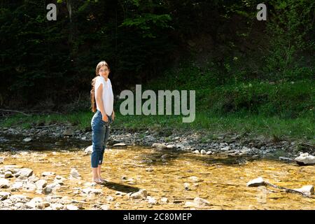 Girl goes barefoot on the stones of a mountain river. Girl`s feet in water